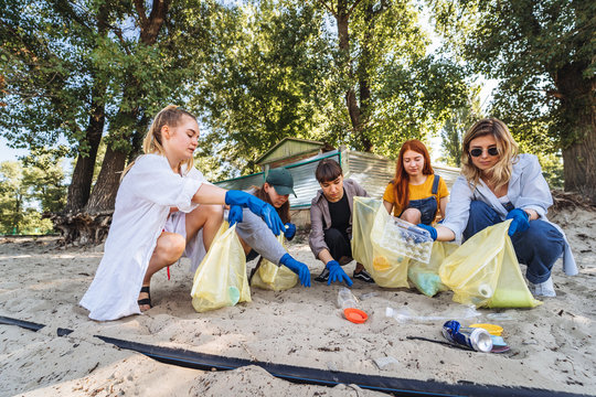 Group of activists friends collecting plastic waste on the beach. Environmental conservation.
