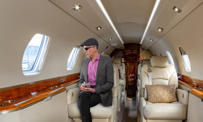 Confident mature man sitting at his seat in private airplane holding a drink.