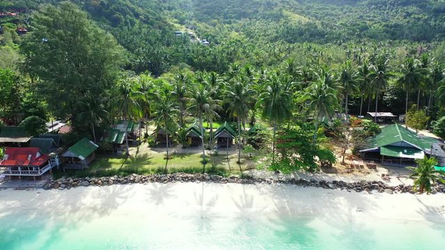 Beach cabins and bungalows with sea view built on quiet shore of tropical island under palm trees on tropical island in Thailand