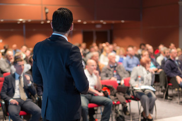Speaker giving a talk on corporate business conference. Unrecognizable people in audience at...