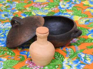 A water clay jug (“moringa” in Brazil) and an empty clay pot with lid, handicraft of Brazilian indigenous origin, on a very colorful “chitao” fabric with large floral prints.