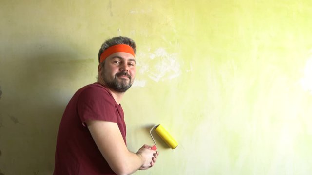 Bearded man against the wall. Good mood. In the hands of a construction roller for wallpaper. Repair work in the room. Frick. Retro style. Green wall.