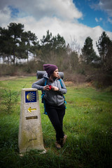 a pilgrim woman rests leaning on a sign of the Camino de Santiago