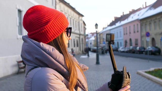 a girl in a red hat shoots a video on a gopro that stands on a selfie stick