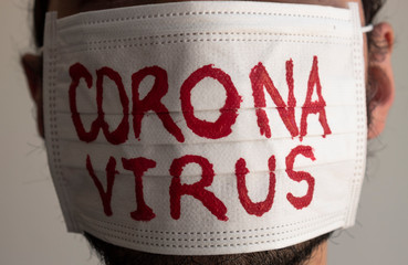 Closed up to a CORONAVIRUS man patient with beard using a white face mask with red CORONAVIRUS inscription. Concept photography COVID-2019