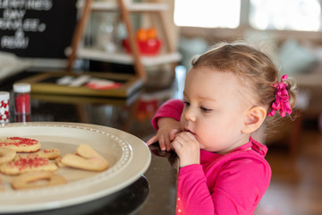 Cute toddler girl eyeing a plate of cookies