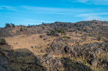 Paisaje montañoso y rocoso al atardecer con personas practicando senderismo. 
