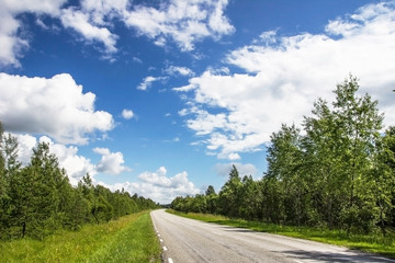 Long empty asphalt road in Europe. Forest and green meadow field in Estonia. Cloudy blue sky.