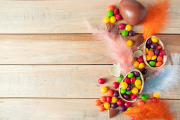 Composition of chocolate Easter eggs and feathers on a light background. Multi-colored sweets for the holiday.