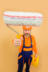 Bearded repairman in uniform holds paint roller. Repair man full height. Professional painter. Designer, builder, worker in hard hat. Painting concept. Bearded man in working clothes with roller.