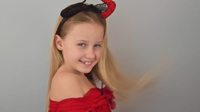 Slowmotion beautiful pretty positive caucasian girl in a red dress and devil horns demonstrates her beauty on a gray background. Concept of the future fatal beauty