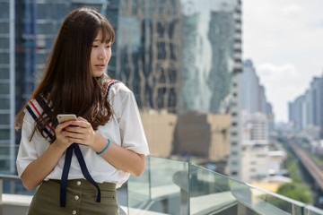 Young beautiful Asian teenage girl using phone against view of the city