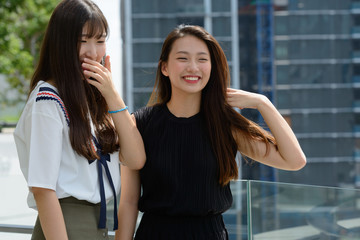 Two young beautiful Asian teenage girls together against view of the city