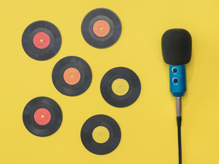 Blue microphone and six vinyl discs scattered on a yellow background.