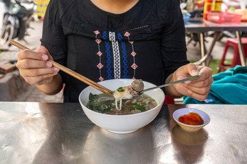 Asian tourist eating Pho noodle soup with chopsticks and spoon