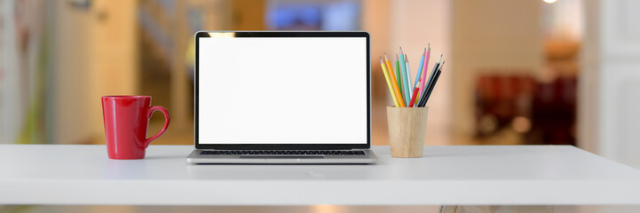 Cropped shot of simple workspace with blank screen laptop, red mug, stationery and copy space