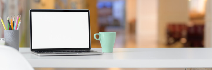 Cropped shot of simple workspace with blank screen laptop, mug, stationery and copy space