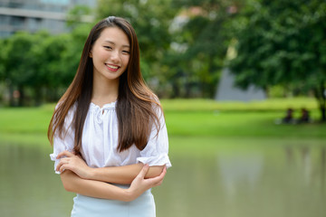 Happy young beautiful Asian teenage girl smiling with arms crossed at the park