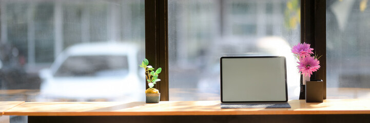 Cropped shot of working space with blank screen tablet and flower vases on wooden counter bar
