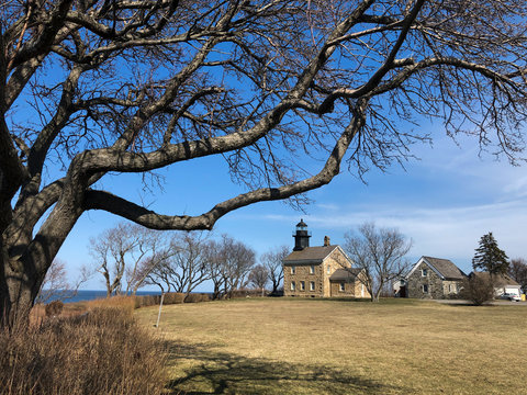 Title: The Old Field Point Lighthouse in the Distance with Tree Branches in the Foreground on a Sunny Winter Day in Setauket, Long Island, NY