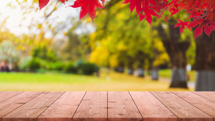 Naklejka na ściany i meble Empty wood table top and blurred autumn tree and red leaf in the park banner background - can used for display or montage your products.