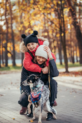 Happy mother and her daughter playing with dog in autumn park