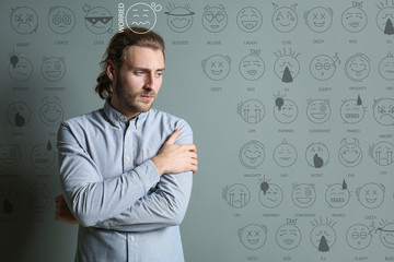 Portrait of worried young man with drawn emoticons on grey background