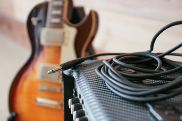 Modern amplifier and guitar near wooden wall, closeup