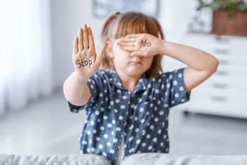 Little girl with words STOP and NO on her palms at home. Concept of violence