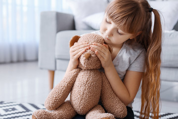 Little girl covering eyes of toy bear at home. Concept of violence
