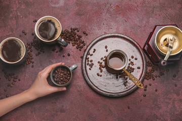 Female hand, cups of different coffee, jezve and grinder on color background