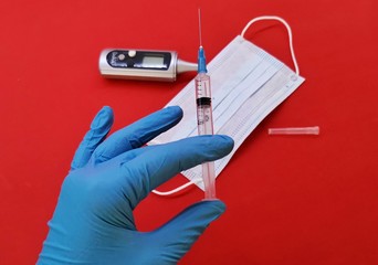 A gloved hand with a syringe on the background of a medical mask, tablets, on a red uniform background, respiratory protection from coronavirus, the epidemic in China, the fight against the virus