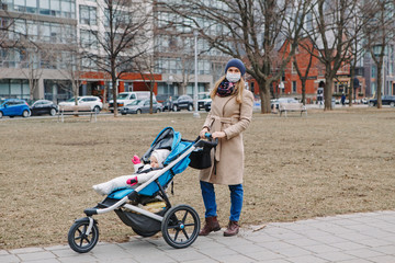Young Caucasian mother in a surgical mask walking with baby outdoor in Toronto. Protective face mask precaution against new Chinese atypical pneumonia COVID-19 epidemic virus disease.