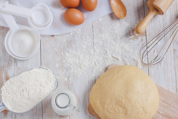 Homemade Dough Recipe (Eggs, flour, milk, sugar) and wooden kneading dough on a wooden table, view...