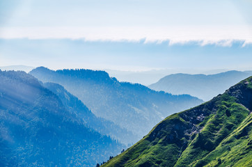 Green mountain slope. Layers of mountains in the haze during sunset. Krasnaya Polyana, Sochi, Caucasus, Russia.