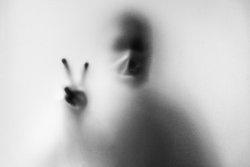 Obraz premium Rozmycie cienia człowieka noszącego maskę, aby zapobiec infekcji. Dłonie palcem do walki na szklanym tle. Walka z chorobami zakaźnymi covid-19. Zamazany obraz. Walka ze śmiertelnymi chorobami zakaźnymi.