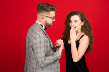 Handsome man in suit proposing to girlfriend in valentine day isolated on red background