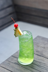 A glass of cocktail is photographed on a wooden table without additional ornamentation.