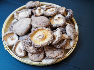 Top view of dried shiitake mushrooms in bamboo tray on black wooden table.