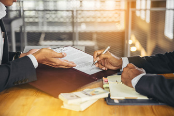 Businessman puts signature on contract at business meeting and passing money after negotiations with business partner. Selected focus