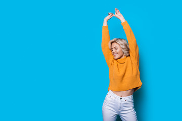 Delightful blond caucasian woman posing with her hands up on a blue background with free space