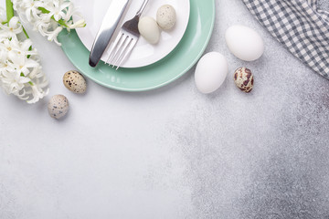 Fototapeta na wymiar Beautiful Easter table setting in Scandinavian style. Green mint plate, eggs, hyacinth and silver cutlery on stone background. Copy space. Top view