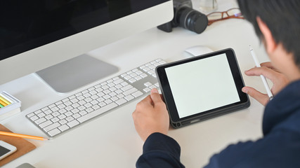 Cropped shot of smart man holding stylus pen in hands while using white blank screen computer...