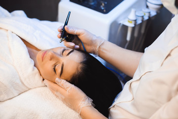 Upper view photo of a face treatment with modern apparatus on the face of charming caucasian lady...