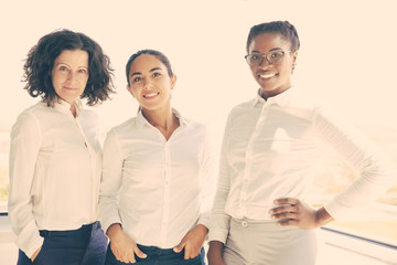 Happy female business team posing together near office window. Businesswomen standing for camera and smiling. Successful team concept