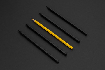 Yellow pencil among black pencils on the matte black background. Minimal style. Conceptual minimalist black art. Matte surface. Office supplies