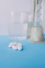 A handful of large white capsules of tablets against the background of laboratory medical devices, glass glasses and a beaker.