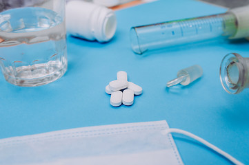handful of large white capsules with tablets on the background of laboratory medical devices, glass glasses with water, beaker and medical mask. Ready layout coronavirus covid-19.