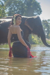 Beautiful thai women wearing traditional thai clothes standing on an elephant in nature park thailand, woman concept