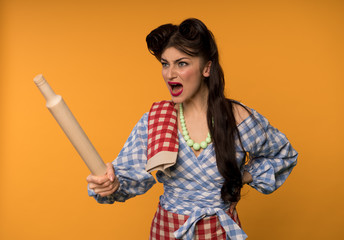 Aggressive pin up woman holding rolling pin and yelling isolated on yellow background
